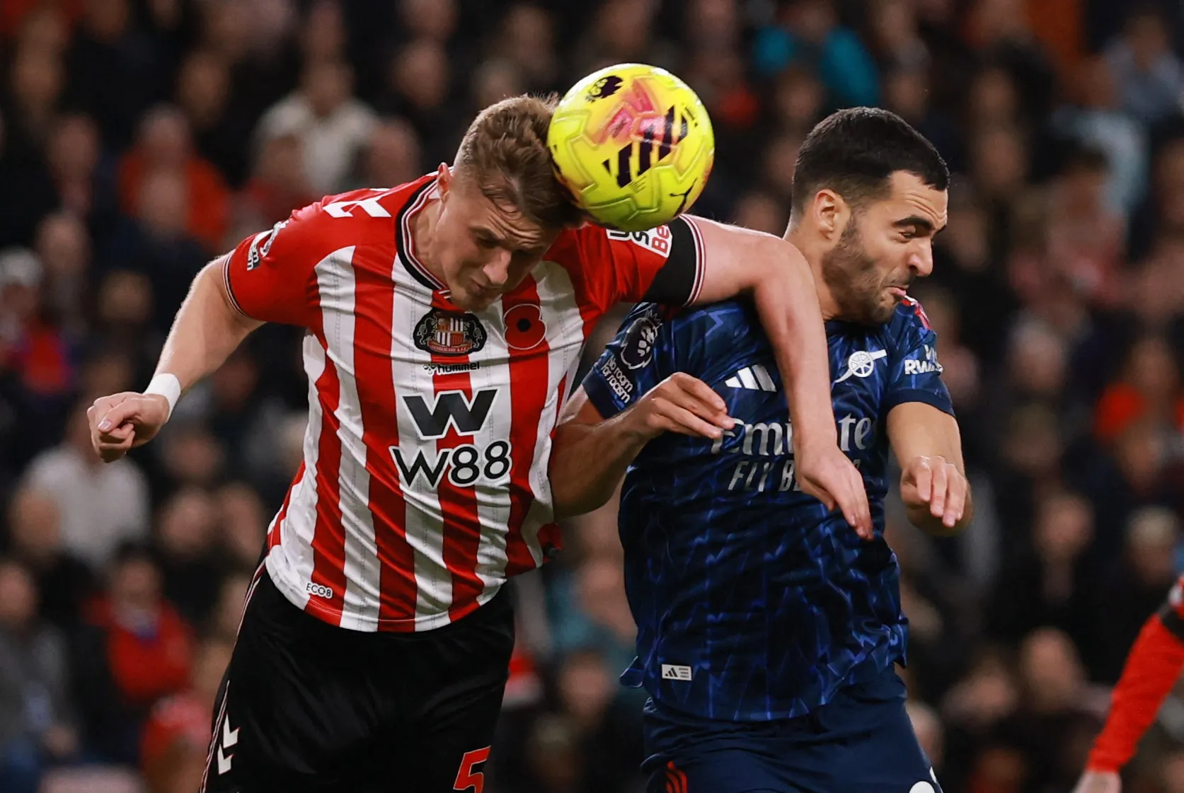 لاعبا كرة قدم يرتديان قمصانًا حمراء/بيضاء وزرقاء يوجهان الكرة.