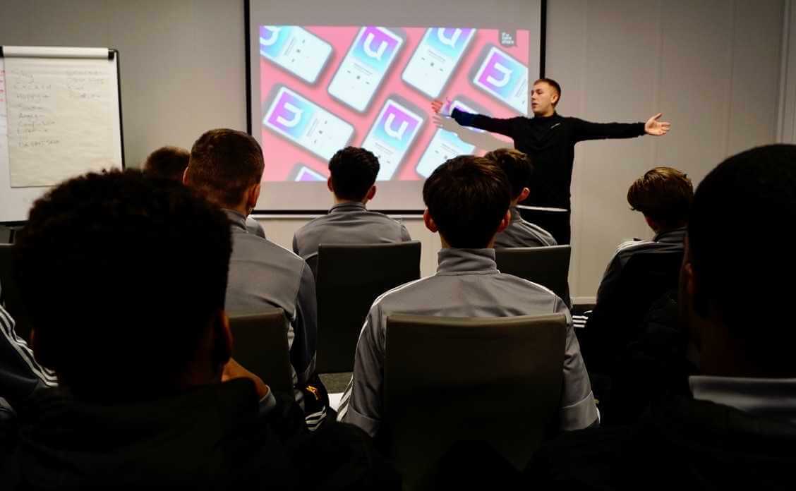 ماثيو سميث، ذراعيه مفتوحتين، يخاطب غرفة مليئة بلاعبي فريق الشباب